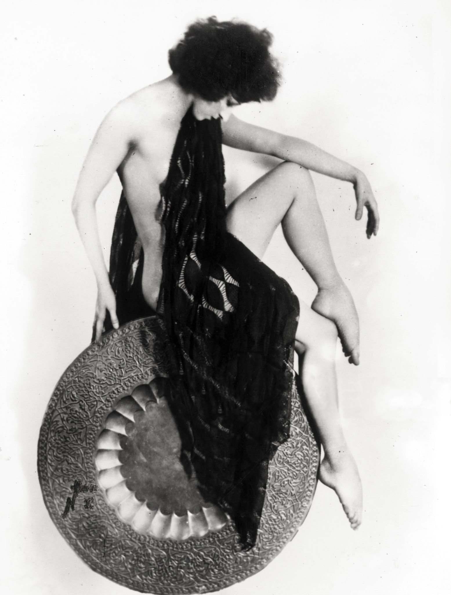 Russian dancer Natacha Nattova balancing on a round decorated object, draping a black veil from her chin, January 1929. (Fox Photos) | src Getty Images